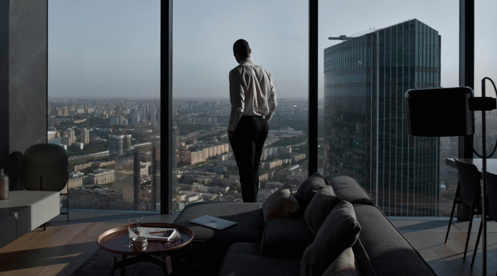 Pessoa observando a cidade de uma janela panorâmica em um studio moderno, representando o conceito de hybrid living urbano com conforto e praticidade.